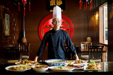 young asian chef displaying his special traditional gourmet on the table in an oriental restaurant setting. dinner for family. chinese new year ambiance. kitchen work. professional cook.