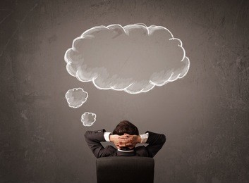 young businessman sitting in office chair in front of a wall with cloud thought sketched on a chalkboard above his head