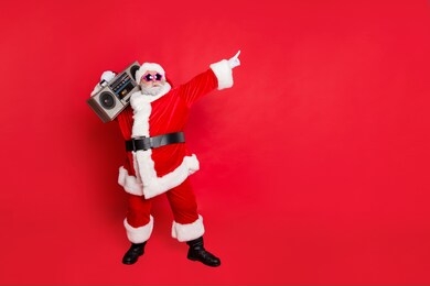 full body photo of funny cute santa claus with sound boom disco box dancing wearing style eyeglasses eyewear headwear hat isolated over red background