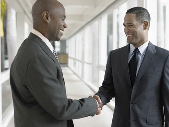 happy african american businessmen shaking hands while standing in office corridor