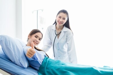 asian young female patient on bed showing thumbs up with smiley face very good symptom to asian young female nurse doctor in hospital background.