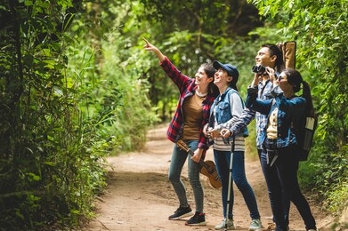 group of asian friends team adventure for hiking and camping in forest together. family travel relaxation. trekking and trail activity in wild life concept. woman pointing at tree or sky. copy space