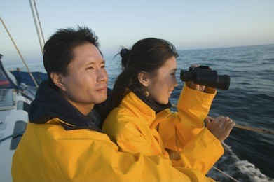 side view of woman looking through binocular with man on yacht