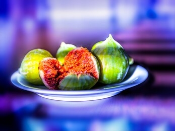 fresh ripe figs on a plate on bright purple neon background