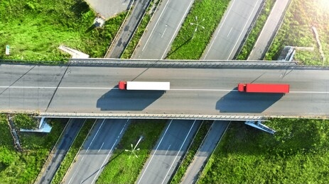 truck logistic aerial. two trucks motion by the highway intersection road between fields. view from drone.