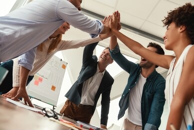 we did it business people giving each other high-five and smiling while working together in the modern office