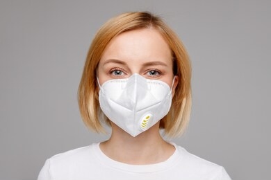 studio portrait of young woman wearing a face mask, looking at camera, close up, isolated on gray background. flu epidemic, dust allergy,  protection against virus. city air pollution concept 