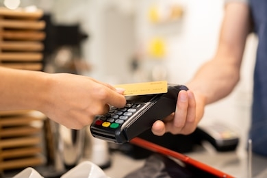 young client of cafe holding plastic card over electronic payment machine held by waiter or barista while paying for food or drink