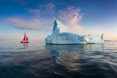 little red sailboat cruising among floating icebergs in disko bay glacier during midnight sun season of polar summer. ilulissat, greenland. unesco world heritage