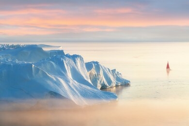 little red sailboat cruising among floating icebergs in disko bay glacier during midnight sun season of polar summer. ilulissat, greenland. unesco world heritage