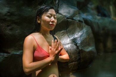 young beautiful and happy asian chinese woman enjoying unique summer holidays at tropical forest meditating doing yoga pose relaxed in natural pool delighted by magical feeling at jungle lake