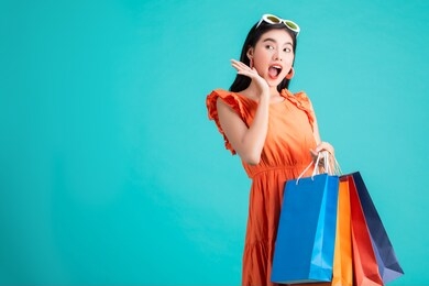 portrait of a happy asian pretty girl holding shopping bags look at away isolated over background,colorful shopping concept.