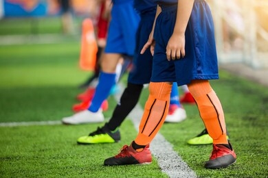kid soccer players standing over white line on green artificial turf ready to training and start game. football or soccer academy.
