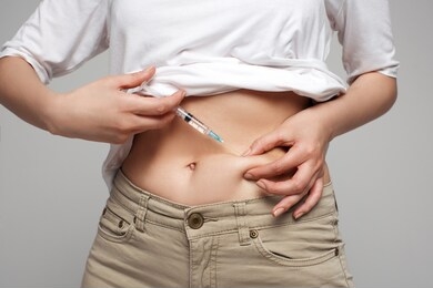studio close up of blonde caucasian woman holding needle making self injection in abdomen, health care, medicine treatment, vaccination, hormonal therapy, in vitro fertilization, isolated background