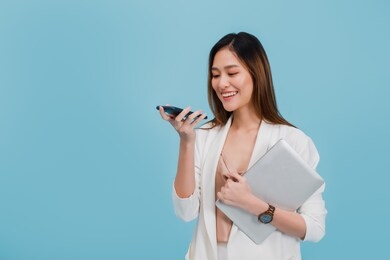 asian beautiful businesswoman make voice call for consulting with smartphone and holding laptop in blue color background with copy space.concept of online business success with technology.