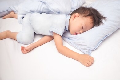 cute little asian 3 - 4 years old toddler boy kid in pajama sleeping / taking a nap on a blue pillow in bed , bedtime for kids concept with copy space
