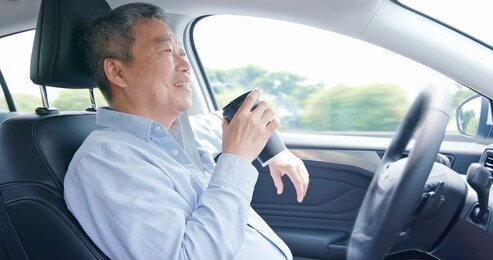 asian elderly man experience self-driving smart car and has a cup of coffee