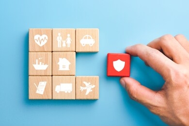 hand holding red wooden blocks with insurance icons. family, life, car, travel, health and house insurance icons, blue background, insurance concept 