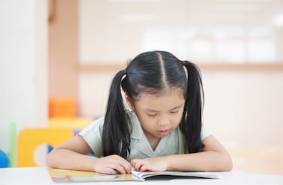 asian child cute or kid girl happy reading story book or student enjoy for learn to tale read with education on colorful chair and table in library classroom at nursery or preschool and kindergarten