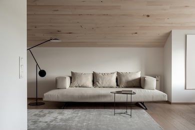 trendy modern interior with a sloping wooden ceiling and white walls and a parquet with a carpet on the floor. there is a sofa with pillows, metal black table with a book, dark floor lamp. horizontal.