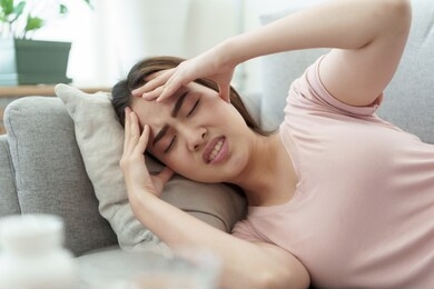 asian woman are holding their hands to the head in pain  sleeping on sofa at home, young women have severe headaches from migraines, health and illness concept