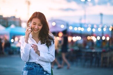 happy young travel asian woman using smartphone and relax on street market against light bokeh background at dusk in bangkok, thailand, travel vacation city concept