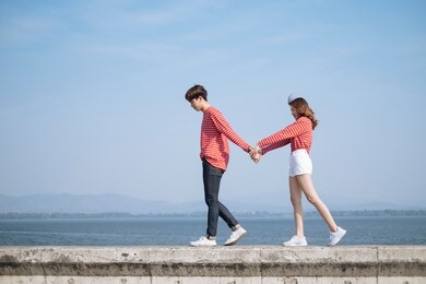 couple holding their hands and walking on the concrete wall.