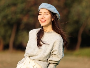 portrait of beautiful chinese young woman in woolen sweater and blue beret smiling with hands in pocket, charming chinese girl with black long hair enjoy her leisure time outdoor.
