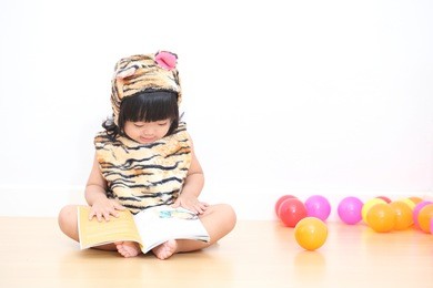 asian baby girl in tiger suit reading a book with colorful ball
