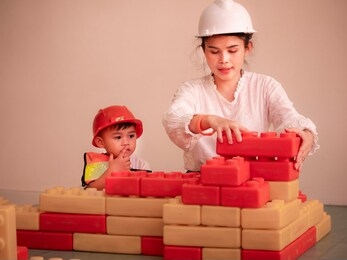 mother and child are helping to build a model house by connecting the lego blocks.