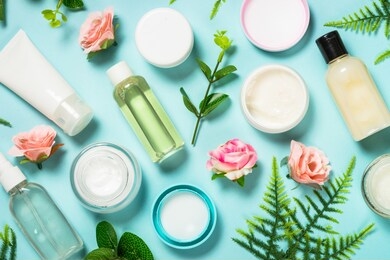 natural cosmetics, skin care product - cream, lotion, soap on blue background with green leaves and flowers. flat lay image with copy space.