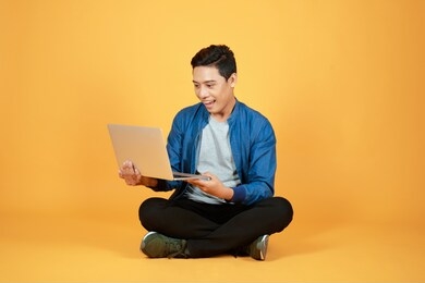 excited happy asian man looking at laptop computer screen and celebrating the achievement isolated over color background