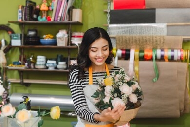 smiling woman florist, small business flower shop owner, at counter, looking friendly at camera working at a special flower arrangement.