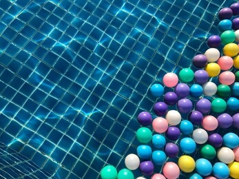 multicolored plastic ball floating on the surface of swimming pool with transparent water, beautiful distorted tiled floor under water and pattern of line, light and shadow from water ripple.