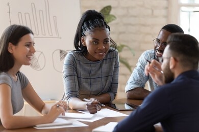 positive successful mixed race group of managers working together at office, sharing project ideas, writing down notes, preparing financial documentation, developing marketing strategy together.