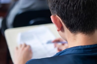 young male student thinking and looking at an important exam at school. 