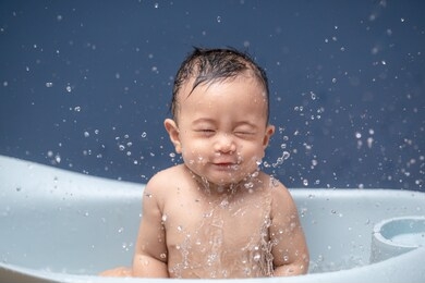 happy little baby taking a bath sitting in bathtub with blue background,hygiene and skin care for young children,clean and healthy concept.