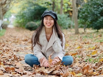 portrait of beautiful chinese young woman in white coat and jeans sitting and smiling in autumn park, charming chinese girl with black long hair enjoy her leisure time outdoor.