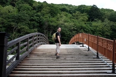 an asian male tourist crossing kisho ohashi - a modern 300 year old cypress (hinoki) wooden bridge in the shape of a japanese drum over the narai river, narai-juku, kiso valley, nagano, gifu, japan.