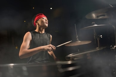 young boy as talented rock band drummer . handsome and cool asian american teenager in headband playing drum kit performing night music show as hobby in teenage  love for music 