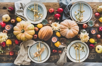 fall table setting for thanksgiving day party or family gathering dinner. flat-lay of plates, silverware, floral and fruit decoration, candle and pumpkins over rustic wooden table background, top view