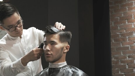 asian male hairdresser cuts clients hair in salon