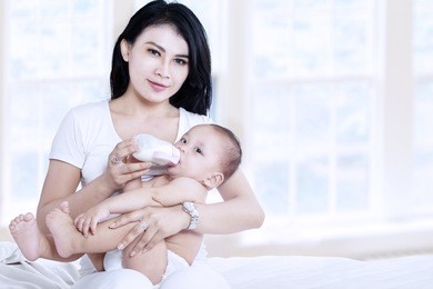 asian mother feeding her baby with milk at home