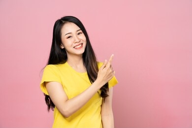 portrait of asian beautiful young woman pointing one hand with finger on upper left side with smile face. the girl standing and looking at camera in studio.  