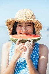 cute asian woman biting watermelon on the beach.