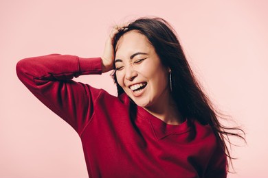 attractive asian woman in red sweater with closed eyes smiling isolated on pink 