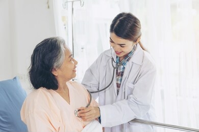 elderly female smiling with young female doctor visiting senior patient woman at hospital ward