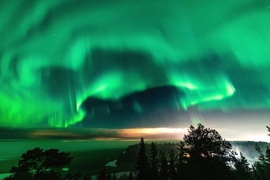 view of brilliant green aurora shining over swedish foggy forest landscape in mountains, light rays from a village and northern lights color sky in different soft colors, northern sweden, scandinavia