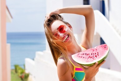 beautiful girl in a swimsuit and sunglasses holds a piece of watermelon at the resort background hotel. happy summer woman