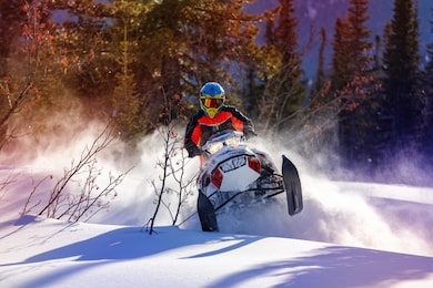 the guy is flying and jumping on a snowmobile on a background of winter forest  leaving a trail of splashes of white snow. bright snowmobile and suit without brands. extra high quality